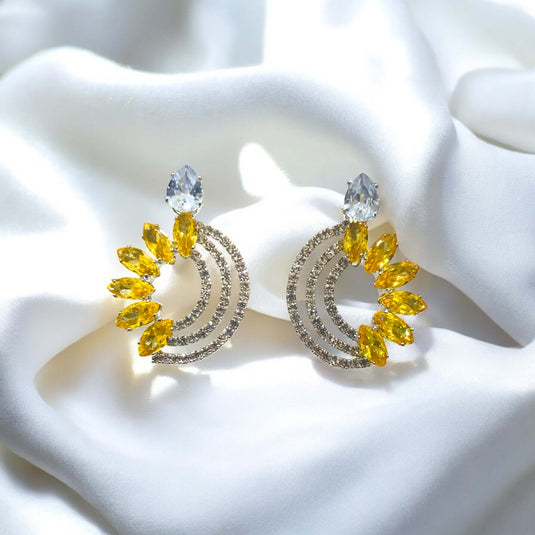 Pair of earrings with yellow gemstones and clear crystals on a white fabric background