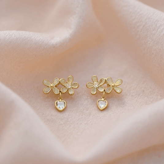 Gold floral earrings with heart details on a soft fabric background