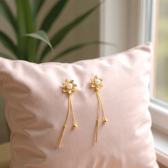 Gold floral earrings on a pink pillow with a plant and window in the background