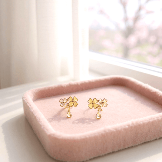 Gold floral earrings on a pink tray with a soft, blurred background