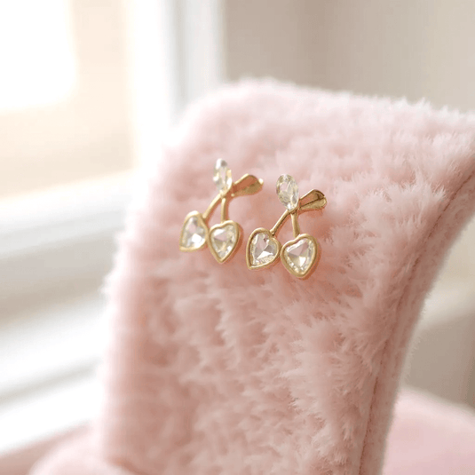 Gold cherry-shaped earrings on a pink surface