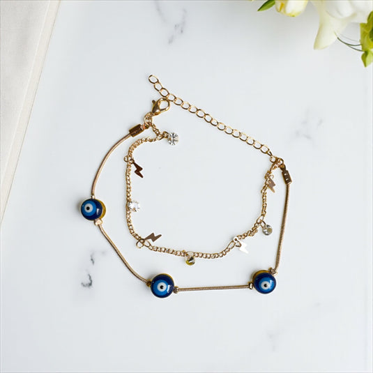Two gold bracelets with blue evil eye charms on a marble surface.