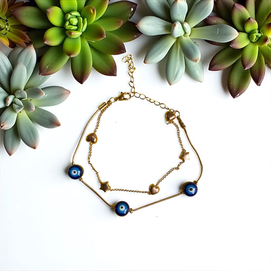Gold bracelet with blue evil eye charms on a white background with succulents