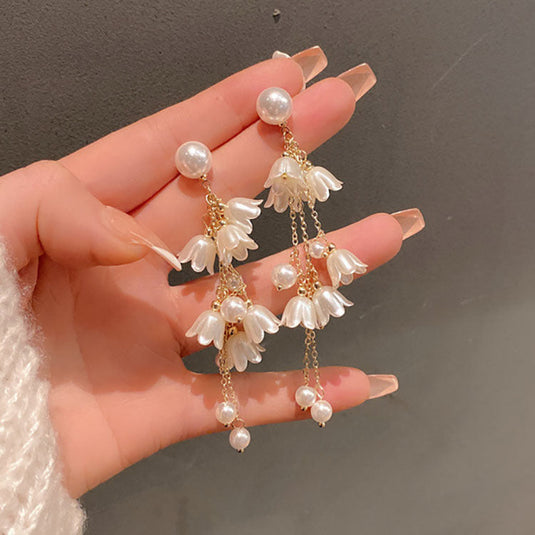 Pearl and flower-shaped earrings held by a hand against a dark background