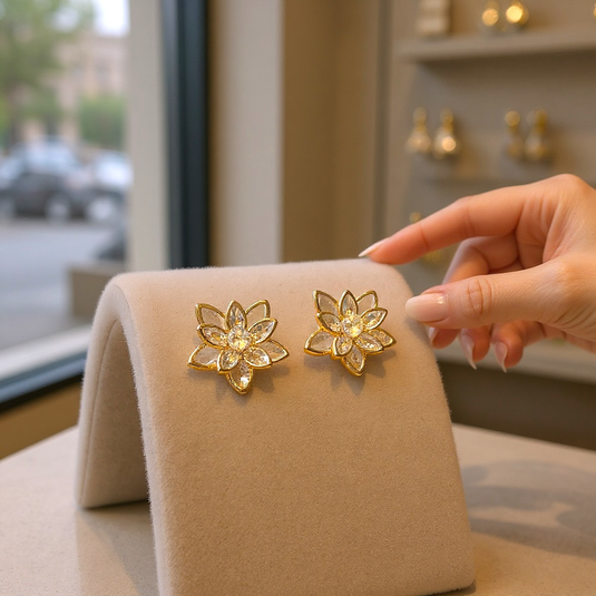 Gold floral earrings on a display stand with a hand pointing at them, blurred background