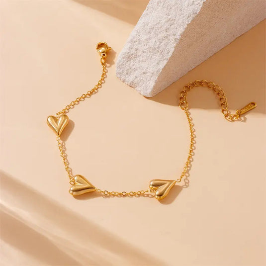 Gold bracelet with heart-shaped charms on a beige background